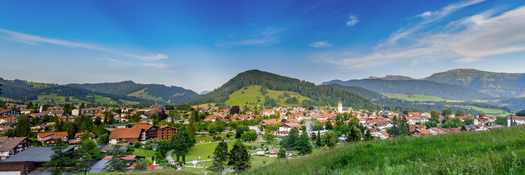 Idyllische Ortsansicht von Oberstaufen im Allgäu mit Alpenpanorama und grünen Wiesen